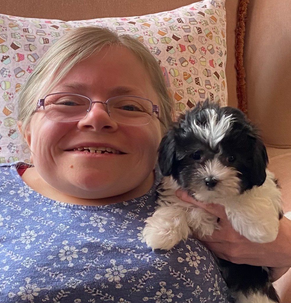 Blonde woman smiling very happily holding a black and white puppy